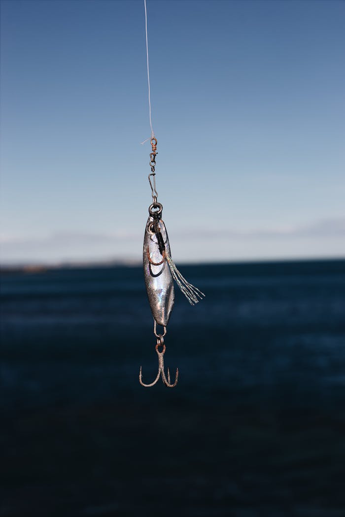 Close-up of a fishing lure hanging against a clear blue sea backdrop, ideal for outdoor and fishing themes.